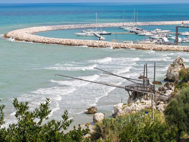 Porto con barche e trabucco sulla costa rocciosa.