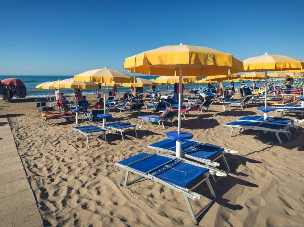 Spiaggia con ombrelloni gialli, lettini blu e persone che si rilassano.