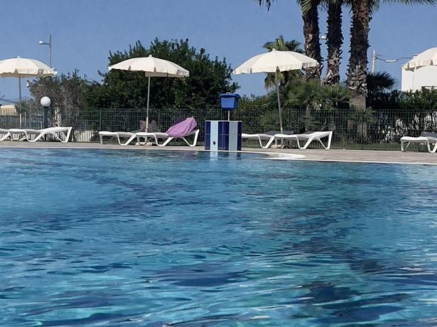 Piscina all'aperto con lettini e palme sotto un cielo limpido.