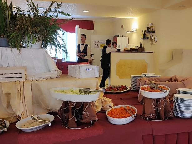 Buffet con piatti e cibo, camerieri sullo sfondo.