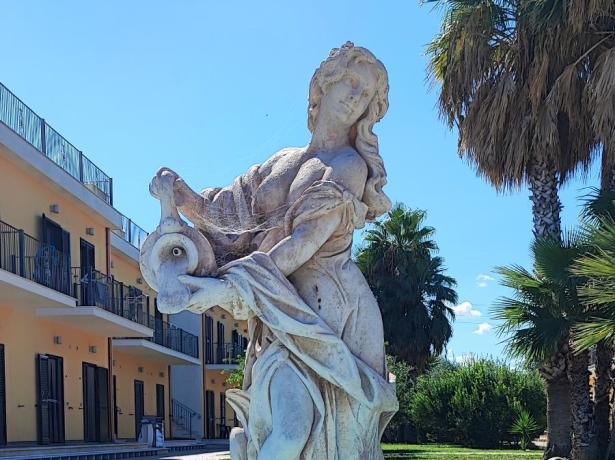 Statua in una fontana con palme e cielo azzurro.