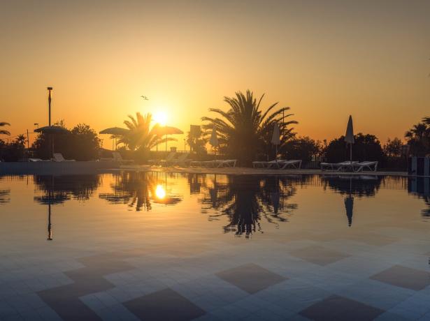 Tramonto su piscina con palme e lettini.