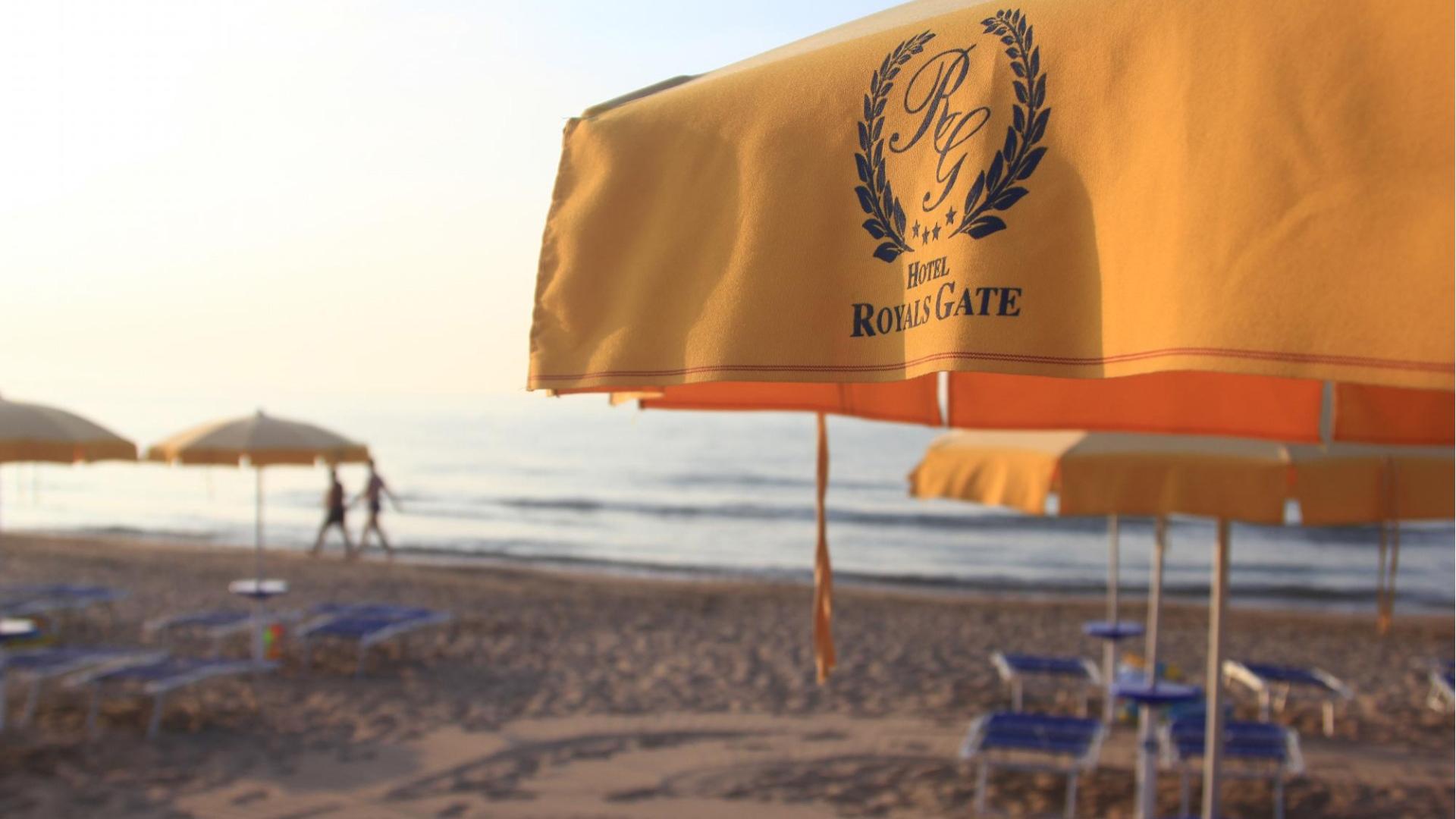 Spiaggia con ombrelloni gialli dell'Hotel Royals Gate, vista sul mare al tramonto.