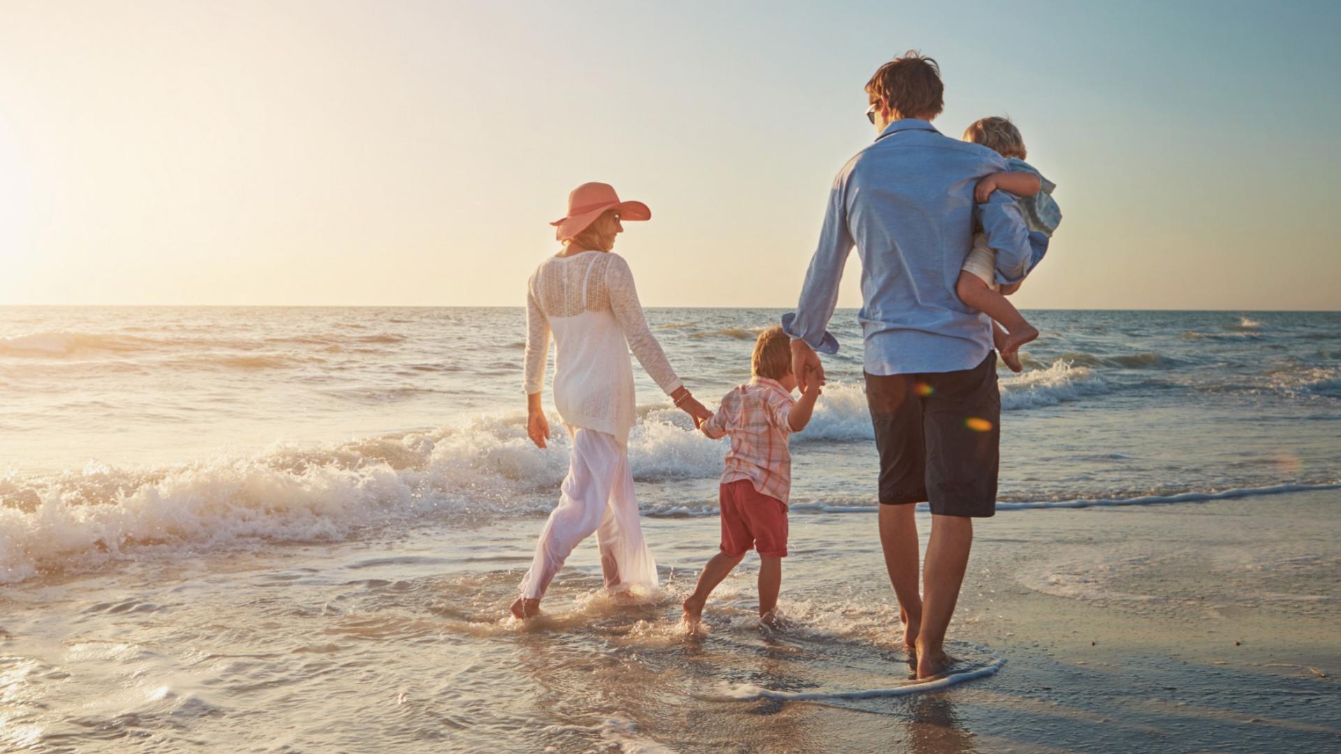 Famiglia cammina sulla spiaggia al tramonto, godendo del mare e della compagnia reciproca.