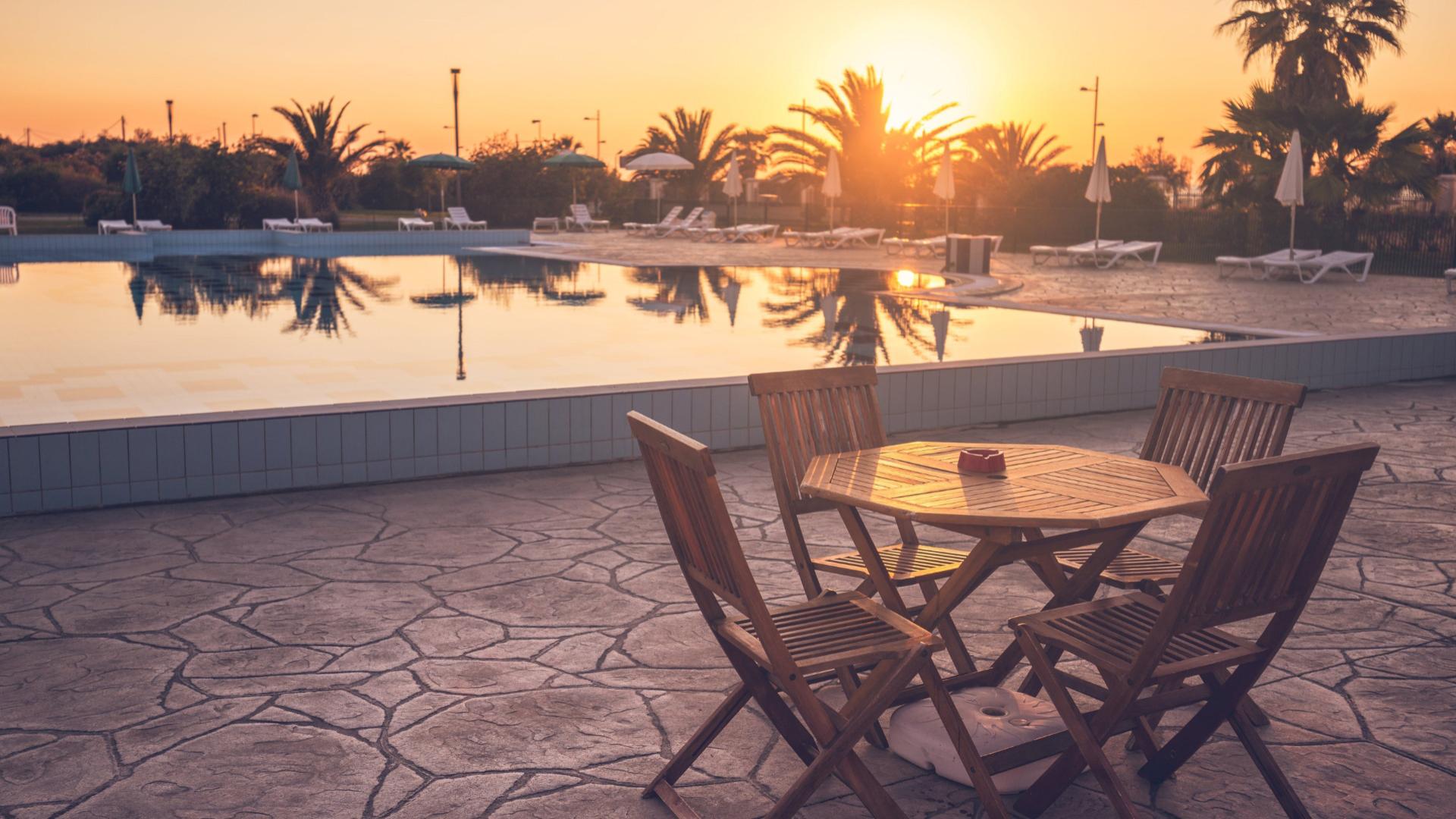 Piscina all'aperto con sedie e tavolo in legno al tramonto.