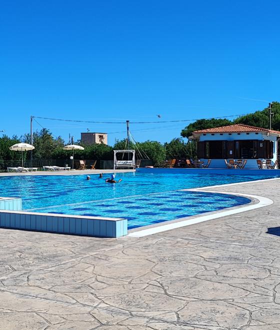 Tavolo apparecchiato a bordo piscina con vista su un edificio e giardino.
