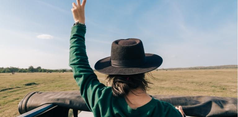 Persona con cappello nero fa il segno della pace in un'area aperta.
