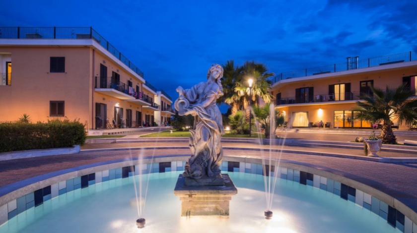 Fontana con statua in un cortile illuminato di sera.