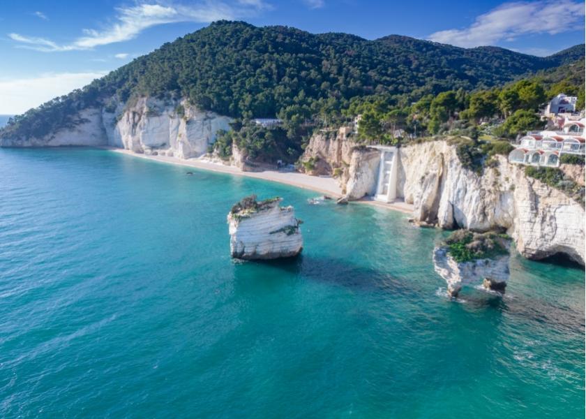 Spiaggia con scogli bianchi e mare cristallino, circondata da colline verdi.