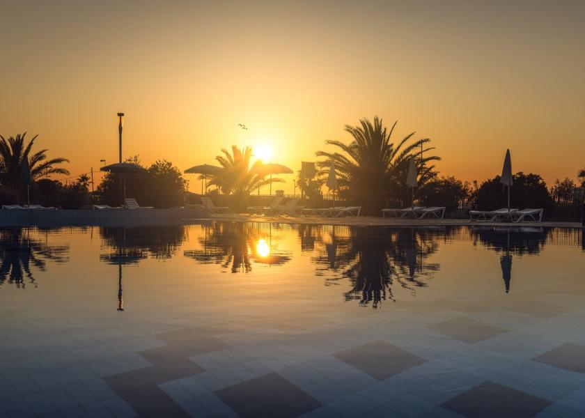 Tramonto su piscina con palme e lettini.